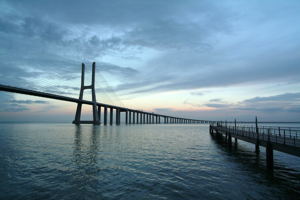To the left is a bridge over the water, to the right is a bridge in the evening twilight.